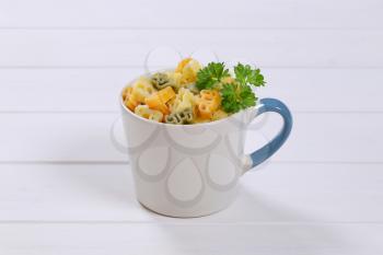 mug of cooked colored pasta on white wooden background