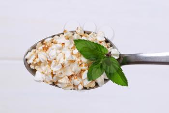 spoon of puffed buckwheat on white wooden background