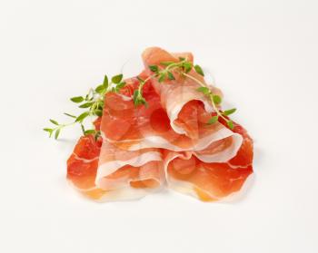 slices of air dried ham with thyme on white background