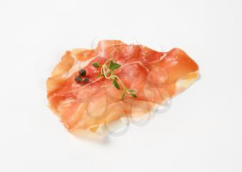 slice of air dried ham with thyme and pepper on white background