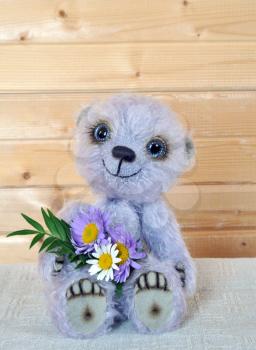 Handmade, the sewed toy: teddy-bear Chupa with a bouquet before a wooden wall