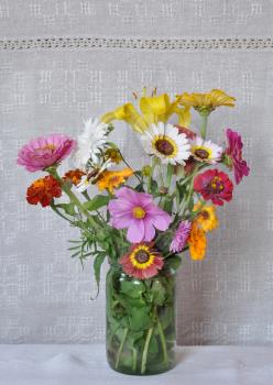 Bouquet of garden flowers in a glass jar on the background of an old linen canvas. August, the Central Russia