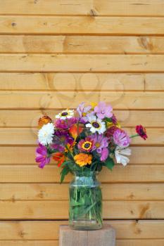 Bouquet of garden flowers in a glass jar on the background of the wooden wall of the old village house