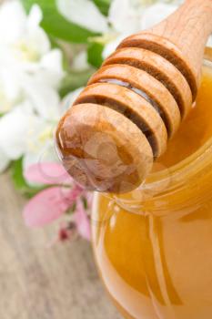 honey in glass and stick with flowerson wood background