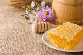 honeycomb, flowers and honey in pot on sacking