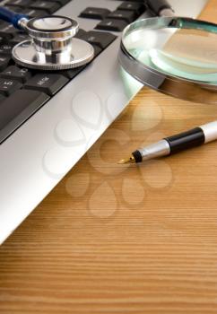 stethoscope and keyboard with pen on wooden table