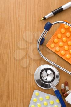 medical stethoscope with pills on wood