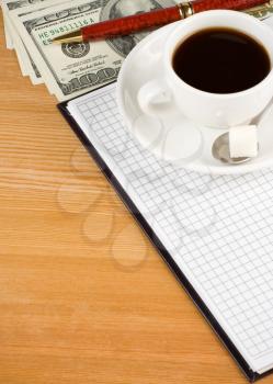 cup of coffee and notebook with dollar on wood table