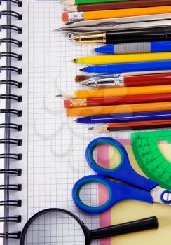 pens, pencils, magnifying glass and other office accessories on cheked notebook