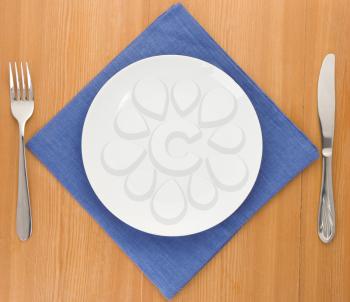 white plate, knife and fork at napkin on wooden background