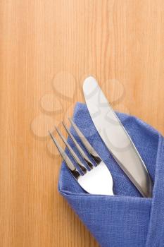 silver fork and knife as utensils in napkin on wooden background