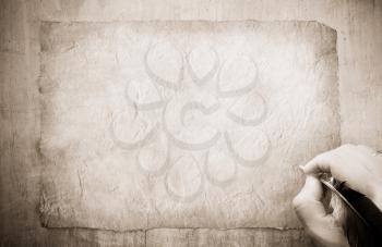 writing hand with feather on old paper parchment background