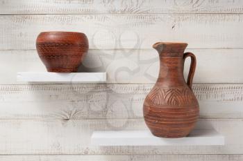 clay jug and pot at shelves on white wooden plank background