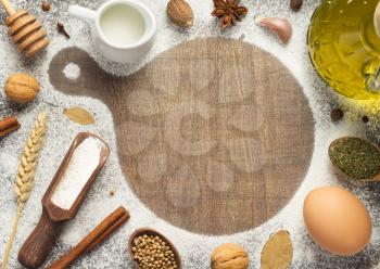 cutting board and bakery ingredients on wooden background, top view