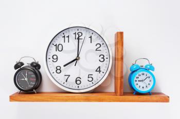 alarm and wall clock at wooden shelf on white background