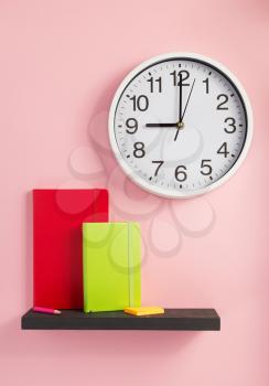 notebook and wall clock on shelf at wall background surface