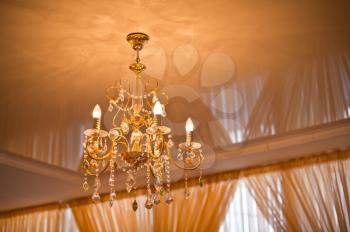 Chandelier on a yellow ceiling and curtains.