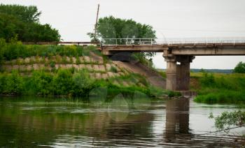 The automobile bridge through the river. Summer landscape of the bridge overgrown with greens.
