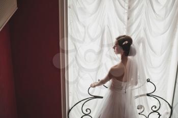 The girl stands up for a curtain at a window.