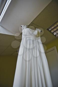 The white dress hangs on a hanger indoors.