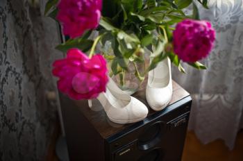 White shoes on a dresser and red flowers.