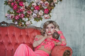 The girl in a pink dress sits on a sofa.
