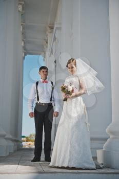 The groom embraces the bride with the white columns.