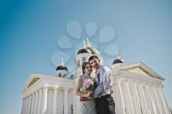 The couple are standing in front of the white columns.