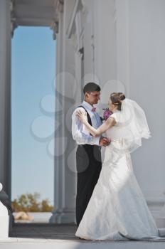 The bride and groom embrace on a background of white columns.