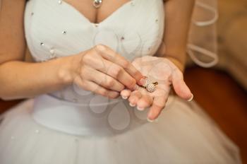 Earrings in hands of the bride and a part of a wedding dress with a big breast.