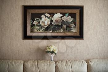 Picture on a wall and a bouquet on a sofa in a room.