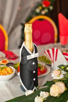 Beautiful bottle in the dress of the groom on a festive table.