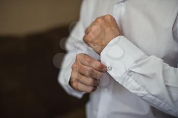 The man clasps a button on a sleeve of a white shirt.