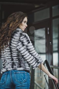 Girl in a fur coat and jeans in the winter on the street.