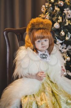 Little Princess in a fur coat around the Christmas tree.