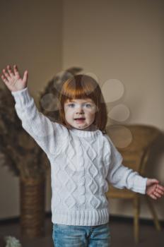A child with red hair in a white sweater.