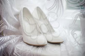 White shoes of the bride on a window sill with a curtain.