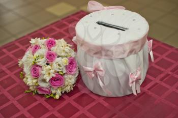 On a table there is a drum for the gifts, similar to a moneybox, and a bouquet.