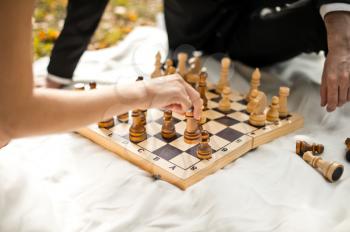The man and the woman play chess outdoors.