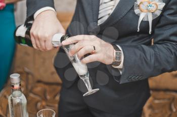 The young man in a suit pours champagne in a glass.