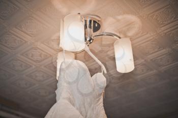 The white beautiful wedding dress hangs on a chandelier.