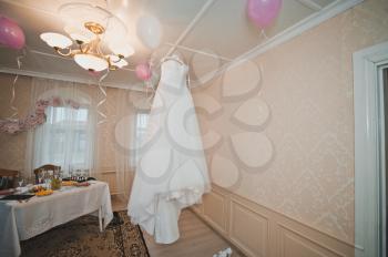 The white beautiful wedding dress hangs on a chandelier.