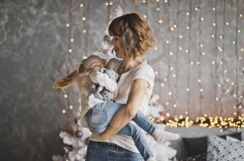 Happy mother holding her daughter in her arms on the background of Christmas decorations.