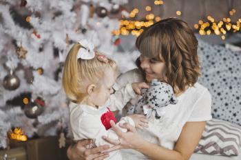 A young mother gently hugs the little girl before Christmas.