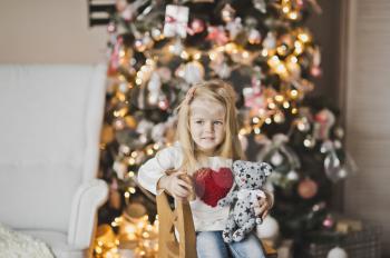Girl with big red heart on the clothes near the Christmas tree.