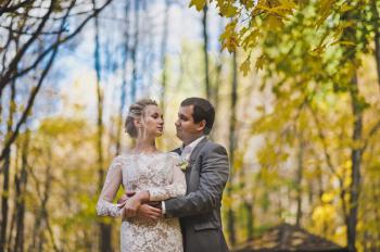 Sunny portrait of the newlyweds standing at the edge of the forest in autumn.