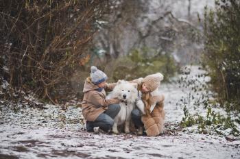 Children on a snowy path playing with the white dog.