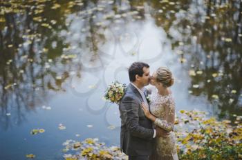 Newlyweds kissing on the background of a lake with autumn leaves.