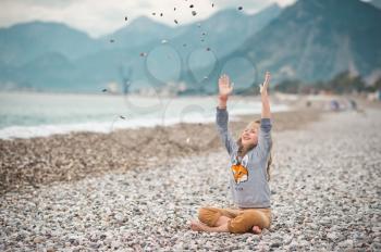 A child throws a pebble sitting on the beach.