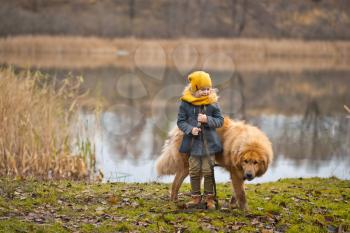 Girl playing with a big guard dog at autumn lake.